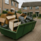 Gevulde afvalcontainer met dozen en vuilniszakken op een oprit in een rustige Nederlandse woonwijk tijdens grote schoonmaak.